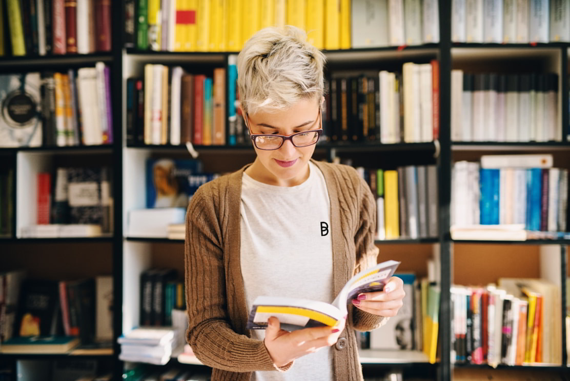 Woman reading a book in a library, representing research, learning, and access to technical knowledge with Ballycatter.